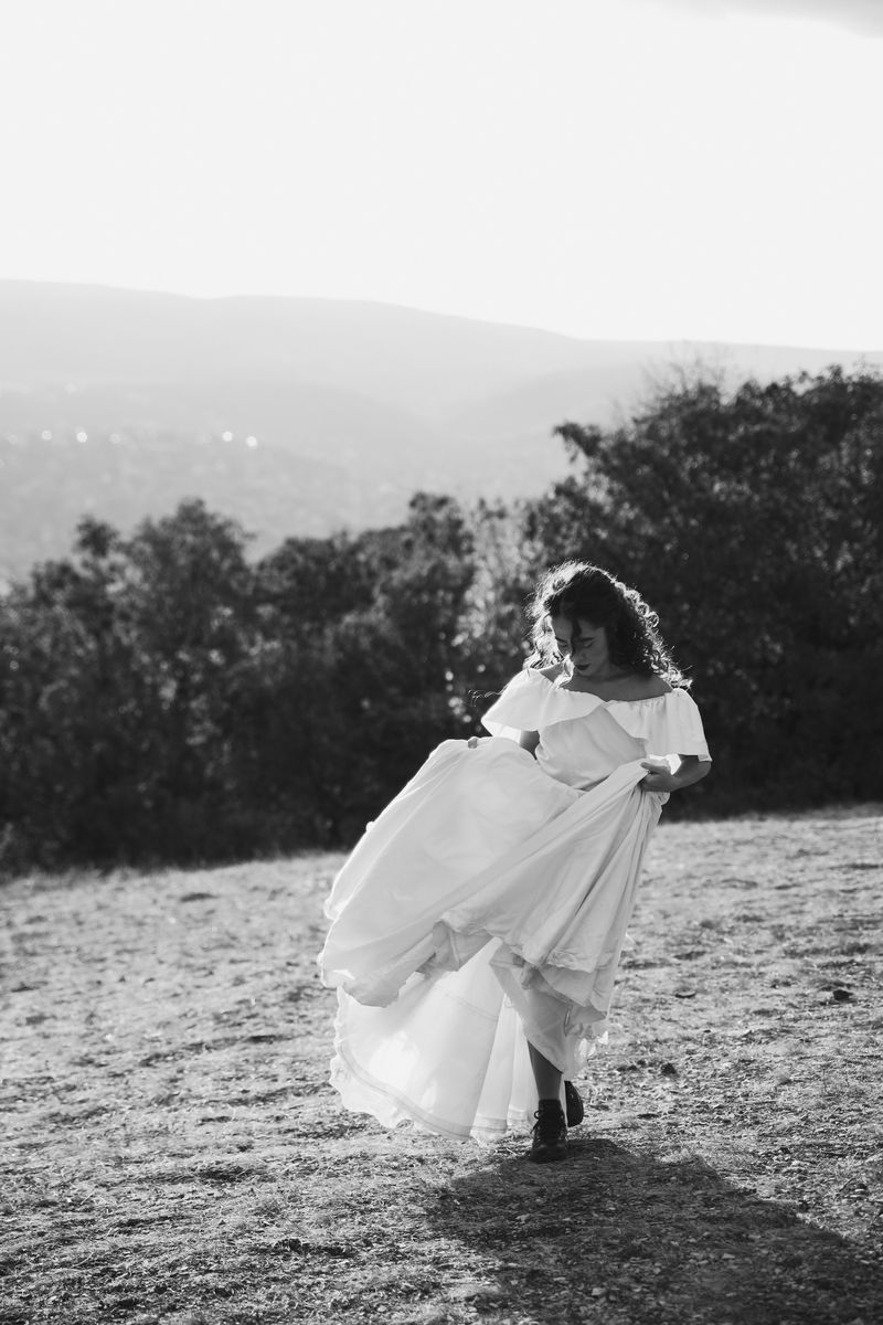 Black and white: a woman in a white dress walking across a hilltop meadow