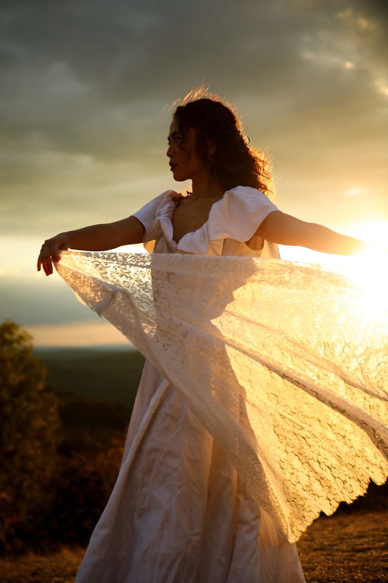 A woman in a white dress spreading a lace skirt into the sunset light
