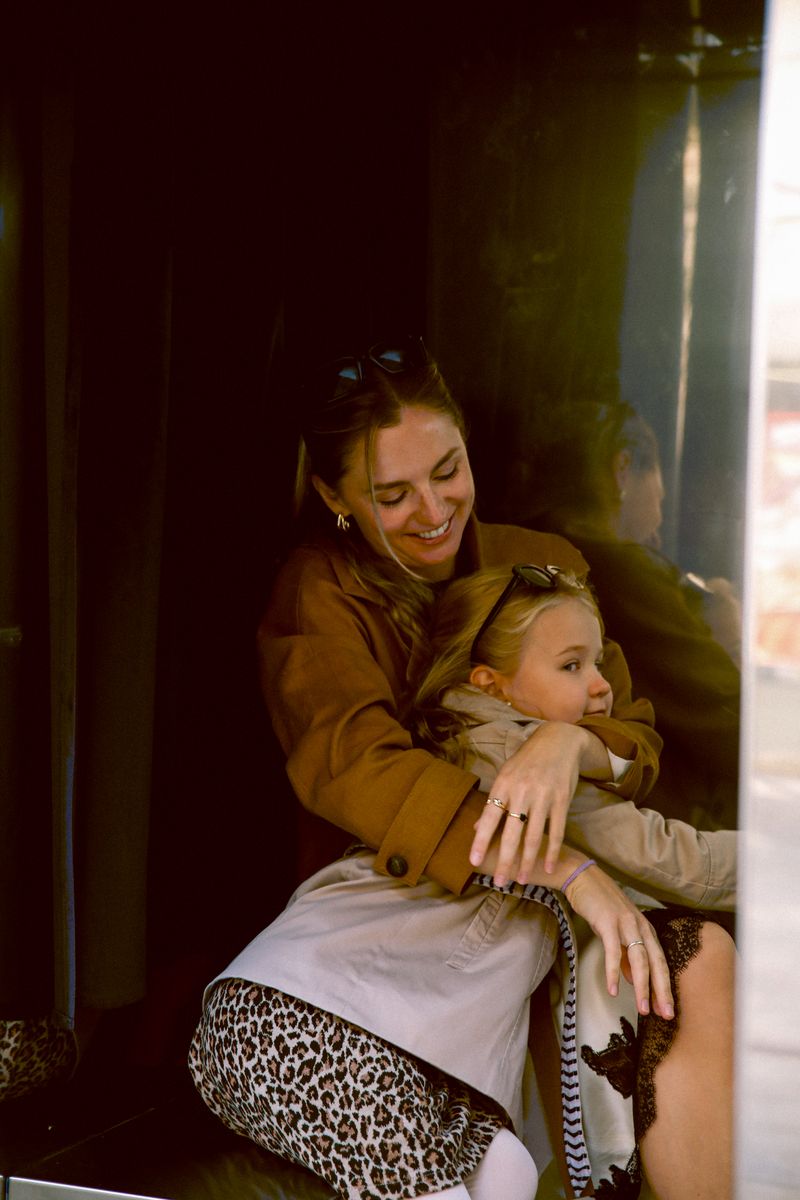 A mother holds her daughter on her lap in a dark doorway, both smiling
