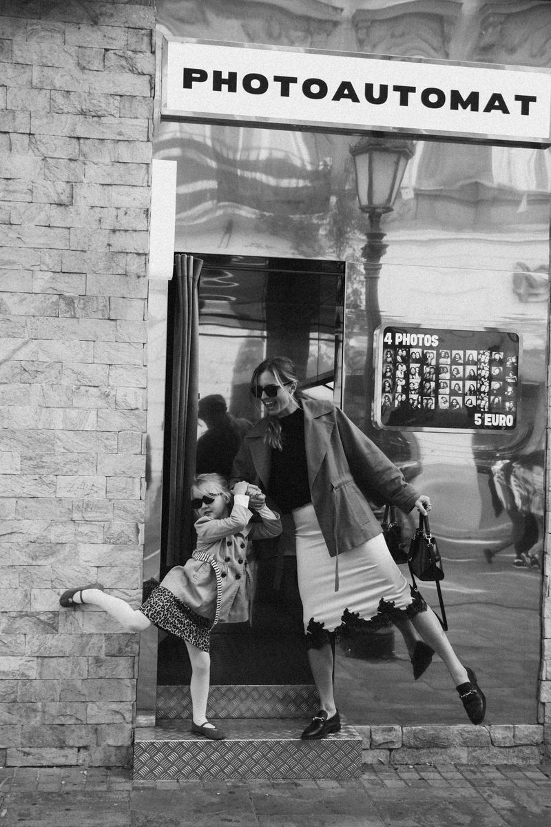 Mother and daughter by a Photoautomat booth, the girl kicking up a leg