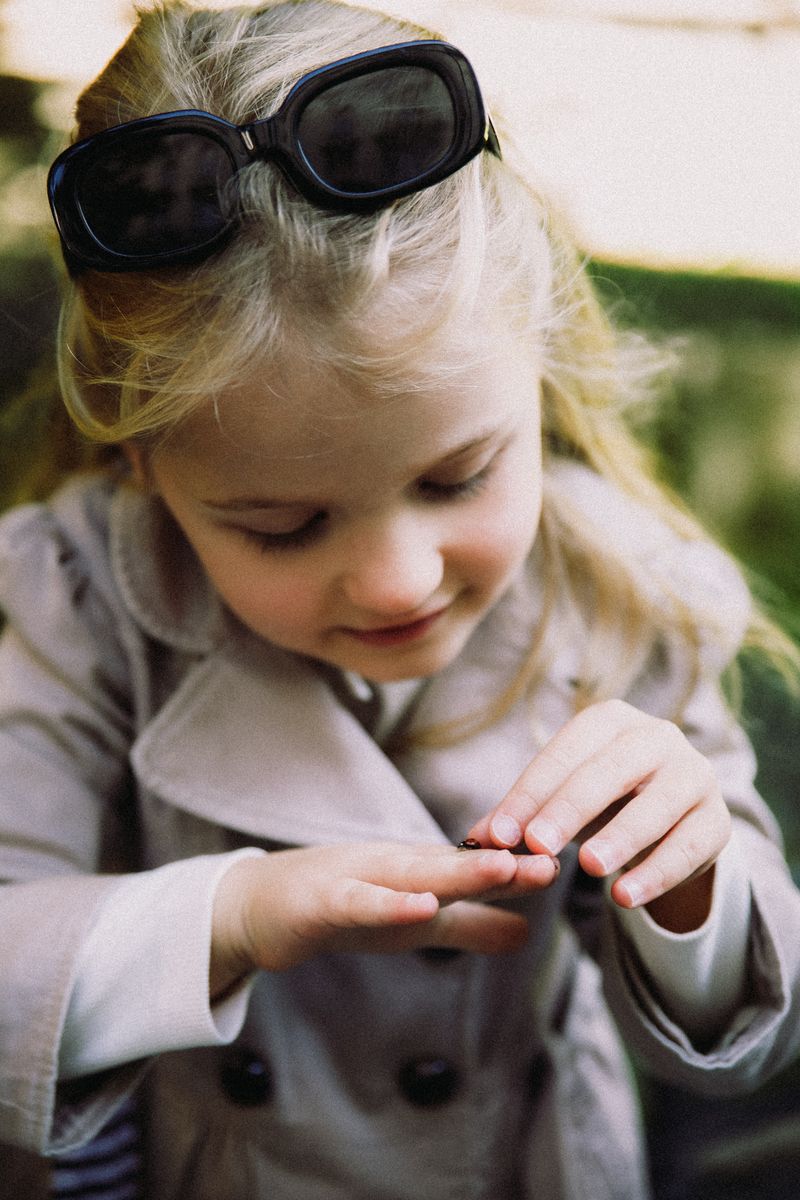 A little girl in sunglasses and a trench coat looking at her hands