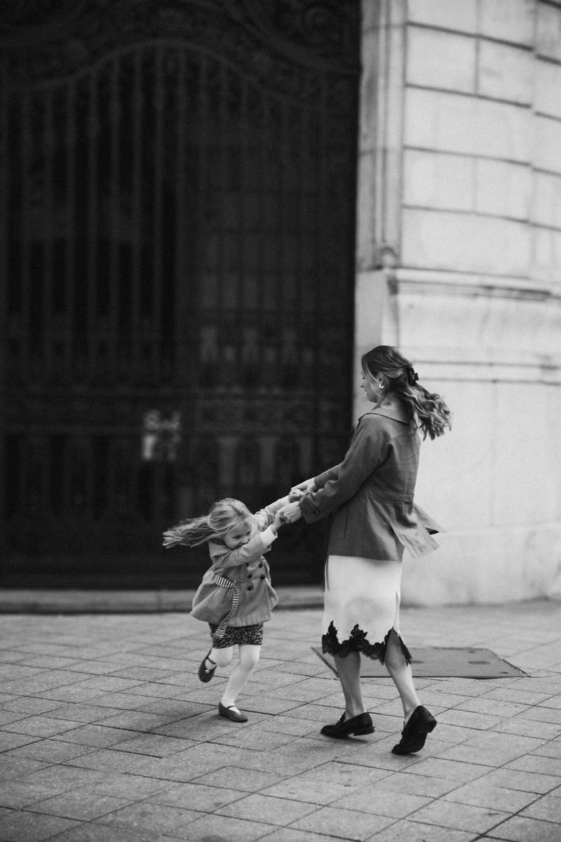 Black and white: a mother spins her daughter by the hands by an iron gate