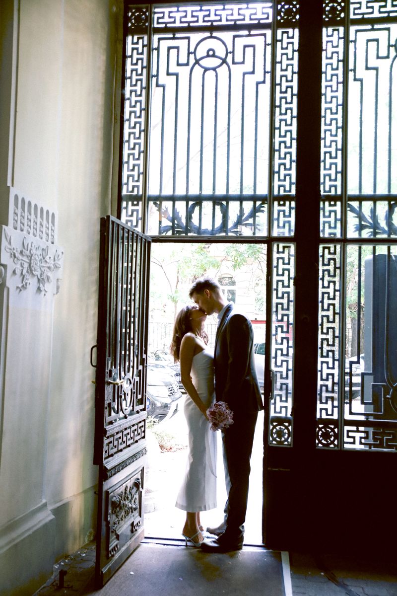 A couple kissing in a doorway in front of an ornate iron screen