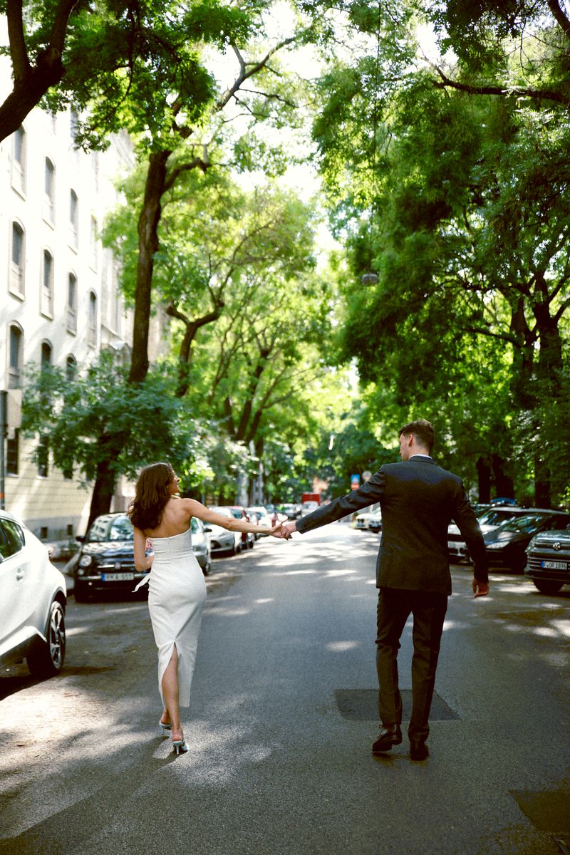 A couple walking hand in hand down a tree-lined city street