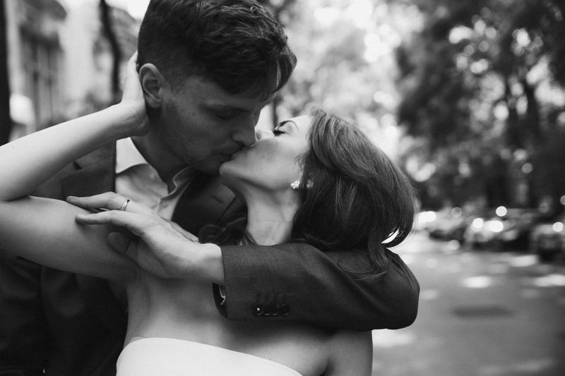 Black and white close-up of a couple kissing on a tree-lined street