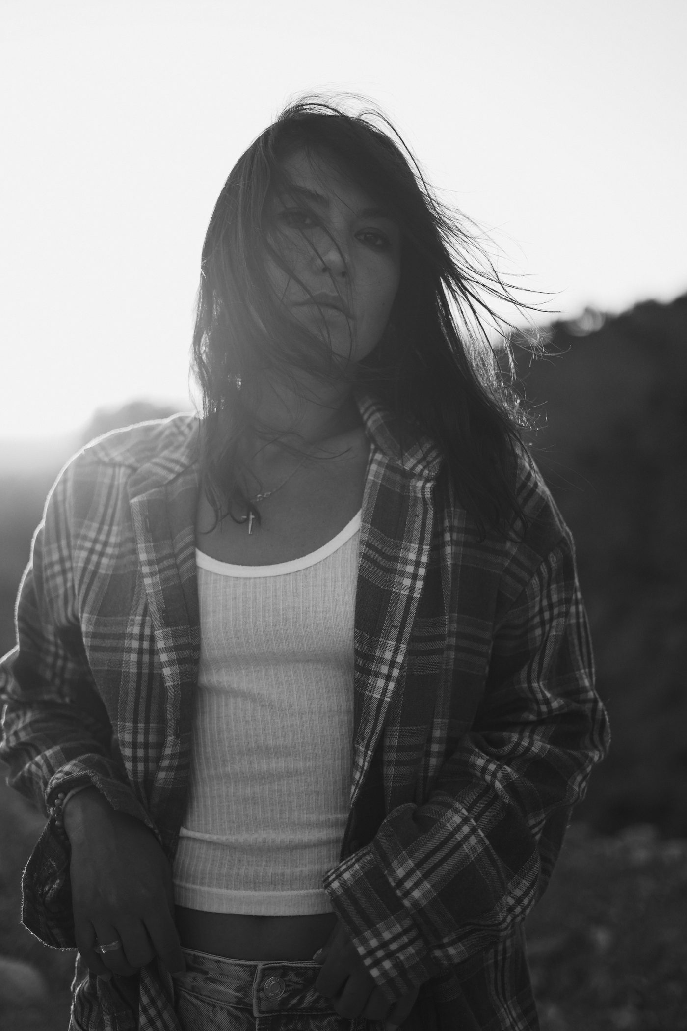 Black and white portrait: a woman in a plaid shirt in backlit evening sun, hair caught by the wind