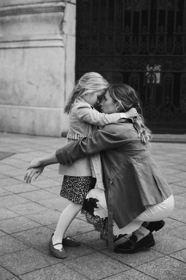 Black and white: a mother kneels on the pavement to hug her daughter